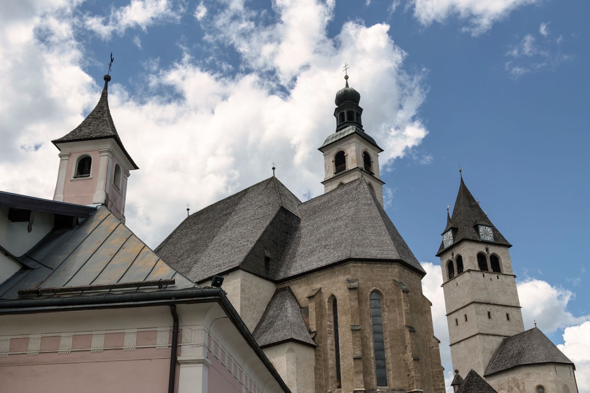 Iconic church spires of Kitzbühel, Austria under a vibrant blue sky with clouds. — photograph by Wolfgang Weiser on Pexels